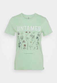 T-shirt en coton vert clair avec le mot "UNTAMED" en blanc, accompagné d'illustrations florales et de texte en dessous, dans une coupe décontractée.