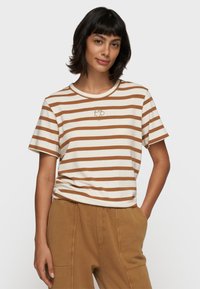 Camiseta a rayas en crema y marrón, de cuello redondo, mangas cortas, con un pequeño logo bordado en dorado en el pecho, hecha de una tela suave.