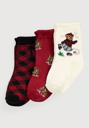 Drei Paar Socken: ein schwarzes Paar mit rotem Rautenmuster, ein rotes Paar mit braunen Schlittbärchen und ein cremefarbenes Paar mit einem Bären auf Schlittschuhen.