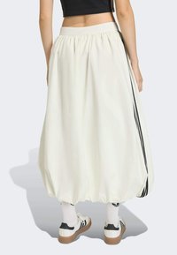 Bijela, široka suknja s naboranim pojasom, koja ima crne bočne pruge, glatku teksturu i voluminozan, balonasti oblik.