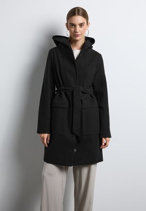 Zwarte jas van een zachte, gestructureerde stof. Heeft een capuchon, een ceintuur in de taille en twee voorzakken. Afgewerkt met een knoopsluiting.