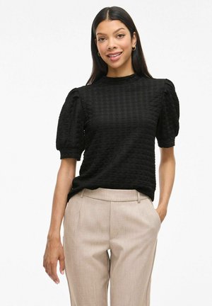 Zwart textuur top met korte pofmouwen, ronde halslijn en aansluitende silhouet, gecombineerd met lichtbeige pantalon.
