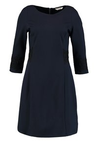 Mörkblå klänning med trekvartsärmar, prydd med blommig spets på ärmarna. Slätt tyg, lätt utsvängd nederkant, dragkedjestängning bak.