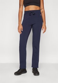 Marinblå träningsbyxor med dragsko i midjan, avsmalnande ben och en textilstruktur. Bärs med svarta träningsskor.