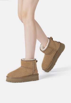 Braune Wildleder-Stiefeletten mit weichem weißen Futter, flachen Sohlen, geschwungenen Oberteilen und minimalen Nähten. Geeignet für Freizeitkleidung.
