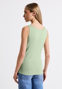 Top verde chiaro senza maniche con scollatura tonda, tessuto in cotone morbido e design aderente. Indossato con jeans di denim blu chiaro.