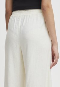 Lichtgekleurde, linnen, wijde broek met een elastische tailleband en een gladde textuur. Beschikt over zijzakken en heeft een ontspannen pasvorm.