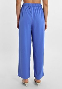 Pantaloni a gamba larga blu con elastico in vita, realizzati in tessuto morbido e elasticizzato. Dettagli visibili alla caviglia con sandali con cinturino.