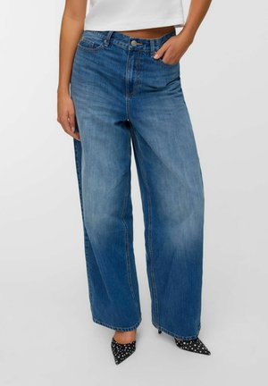 Jeans in denim blu a gamba larga con vita alta, lavaggio sbiadito e design tradizionale a cinque tasche. Abbinati a tacchi neri a pois.