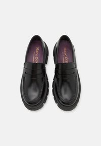 Paire de mocassins noirs en cuir brillant avec semelles épaisses crantées et semelles intérieures violettes marquées "Marc O'Polo", vue de dessus sur fond blanc.