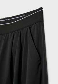 Jupe noire plissée avec ceinture élastique comportant deux fines rayures blanches horizontales sur un fond clair.
