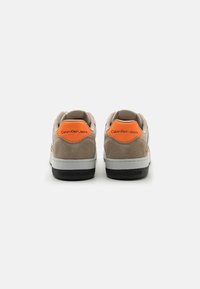 Baskets Calvin Klein Jeans avec dessus en daim marron clair et cuir beige, accent orange au talon, et semelle extérieure en caoutchouc noir arborant le logo.