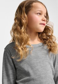 Graues Langarmshirt aus einem weichen, strukturierten Stoff. Das Kind hat hellbraune, gewellte Haare, die über die Schultern fallen. Einfacher, runder Ausschnitt.