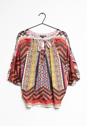 Blouse fluide à manches courtes présentant un motif géométrique multicolore vif avec un col noué à l'avant. Fabriquée en tissu léger, avec un ourlet arrondi.