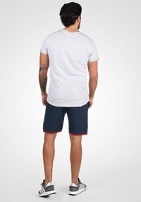 Grijze t-shirt met korte mouwen en een ronde zoom, gecombineerd met marineblauwe shorts met rode accentuering. Model toont de achterkant, staand op een neutrale achtergrond.