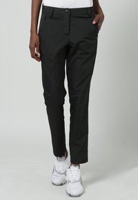 Svarta, slim-fit byxor i ett glatt tyg med knappstängning, sidofickor och dragkedjedetaljer vid vristerna. Bärs med vita sneakers.