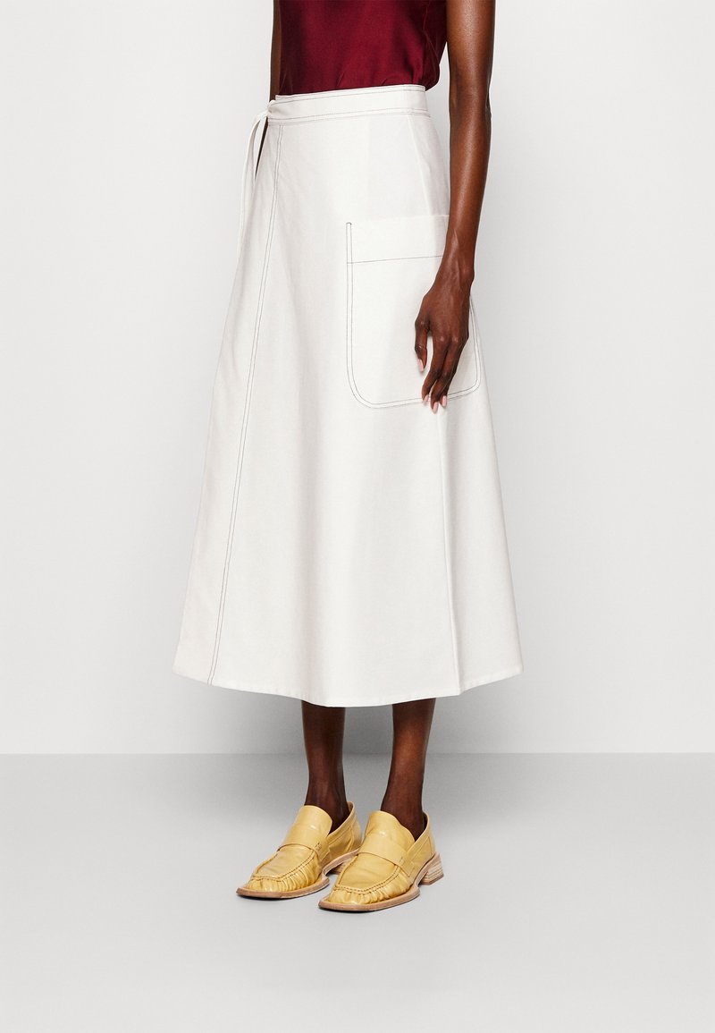 Witte katoenen midi-rok met een strikceintuur, zijzakken en contrasterende stiksels, gecombineerd met gele leren loafers.