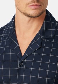 Camisa a cuadros en tonos marinos con cuello, que presenta líneas de cuadrícula blancas y cierre de botón, fabricada en una tela suave con una textura lisa.