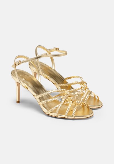 Goldene Riemchensandalen mit hohen Absätzen, die geflochtene Details, ein metallisches Finish und einen schlanken Knöchelriemen aufweisen. Offene Zehenpartie mit einem eleganten Absatz.