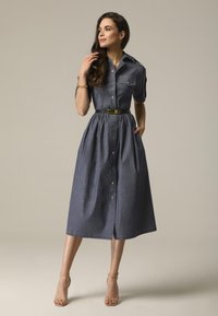 Sukienka dżinsowa z krótkim rękawem, zapięciem na guziki z przodu i talią wciętą. Posiada marszczony dół, kieszenie oraz kontrastowy czarny pasek.