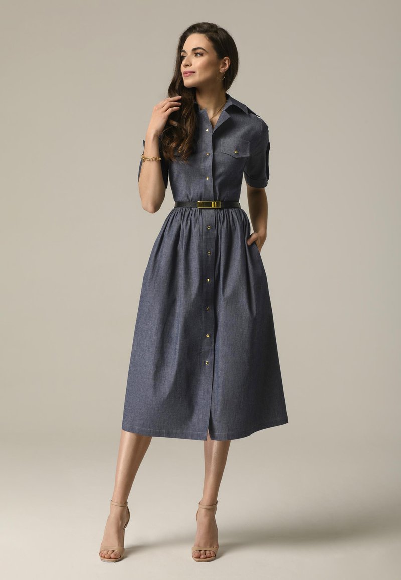 Sukienka dżinsowa z krótkim rękawem, zapięciem na guziki z przodu i talią wciętą. Posiada marszczony dół, kieszenie oraz kontrastowy czarny pasek.