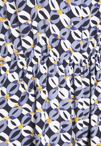 Tissu avec une section froncée présentant un motif répétitif de feuilles abstraites bleues et blanches avec de petites touches orange sur un fond foncé.