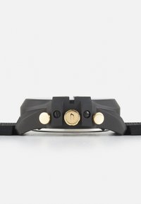 Boîtier de montre gris avec quincaillerie dorée ; comporte un bracelet texturé, un cadran circulaire et un bouton distinct. Design épuré et moderne avec bracelet ajustable.