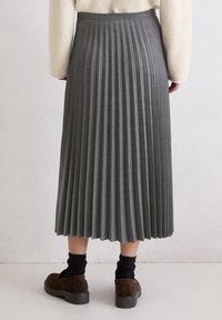 Plissé grijze rok, midi-lengte, gemaakt van een zachte stof. Heeft een aansluitende taille en textuurplooien. Gecombineerd met donkere sokken en schoenen.