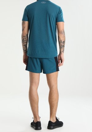 Maglietta sportiva turchese a maniche corte, abbinata a pantaloni corti turchesi e neri. L'outfit è realizzato in tessuto traspirante e ha un design comodo.