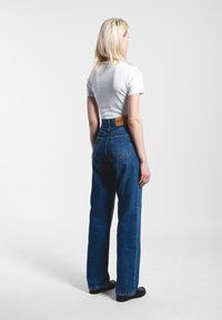 High-waisted blue denim jeans with a straight-leg cut, featuring two back pockets and a brown leather waistband label. Smooth texture.