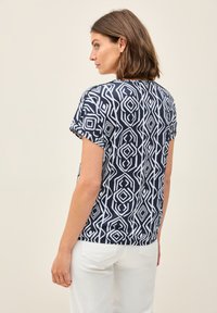 Marinblå t-shirt med vitt geometriskt mönster, korta ärmar, rund hals och avslappnad passform. Matcher med vita byxor. Slät textur.