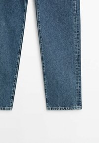 Mörkblå denimjeans med rak benpassform, synlig söm och en lätt blekt textur. Ingen synlig hårdvara eller dekorationer.