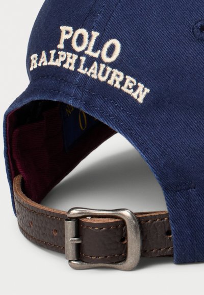 Jūras zila kokvilnas beisbola cepure ar izšūtu "POLO RALPH LAUREN" logo. Iekļauj brūnu ādas siksnu ar metāla sprādzi un bordo oderi.
