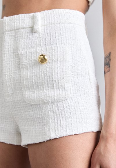 Shorts blancs texturés avec un motif en grille, dotés d'un bouton doré et d'une petite poche à l'avant. Conception décontractée et ajustée.