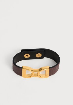 Bracciale in pelle marrone con superficie testurizzata, fibbia doppia Gancini dorata e bottoni a pressione dorati su sfondo bianco.
