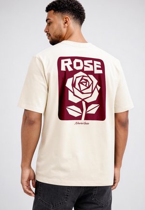 Man wearing beige t-shirt with a large maroon graphic of a stylized rose and the words "ROSE" and "Neverless" on the back.