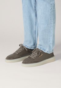 Szare sneakersy z połączenia zamszu i gładkiej skóry; posiadają sznurowadła i kremową gumową podeszwę. Nazwa marki widoczna jest na złoto.