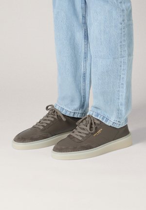 Graue Sneakers aus einer Kombination von Wildleder und glattem Leder; mit Schnürsenkeln und einer cremefarbenen Gummisohle. Der Markenname ist in Gold sichtbar.