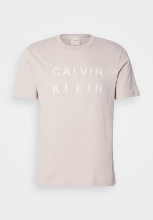 Light pink cotton t-shirt with a crew neck. Features white bold text "CALVIN KLEIN" across the chest. Short sleeves and a relaxed fit.