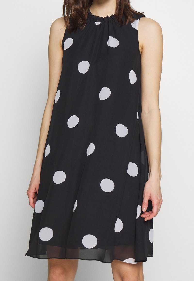Svart ärmlös klänning med en insnörd halsringning, prydd med stora vita prickar, tillverkad av lätt tyg, knälång design.