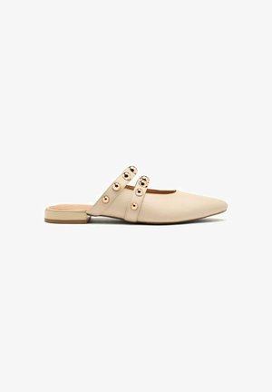 Mules en cuir beige à bout pointu, dotées de deux lanières ornées d'accents métalliques circulaires et d'un petit talon carré. Fini texturé.