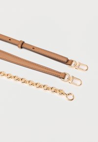 Bandes en cuir tan avec ferrures dorées et détail chaîne; texture lisse, longueur ajustable, avec une fermeture à anneau solide et un fermoir.