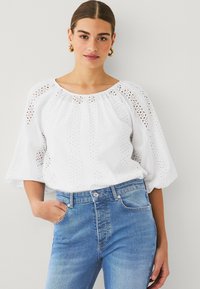 White cotton blouse with eyelet details, puff sleeves, and a round neckline, paired with high-waisted blue denim jeans.