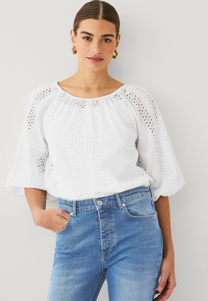 White cotton blouse with eyelet details, puff sleeves, and a round neckline, paired with high-waisted blue denim jeans.