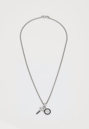 Collier en chaîne argentée avec trois petits pendentifs : une croix, une forme allongée ornée de pierres noires, et un médaillon rond avec une bordure noire et un design complexe.