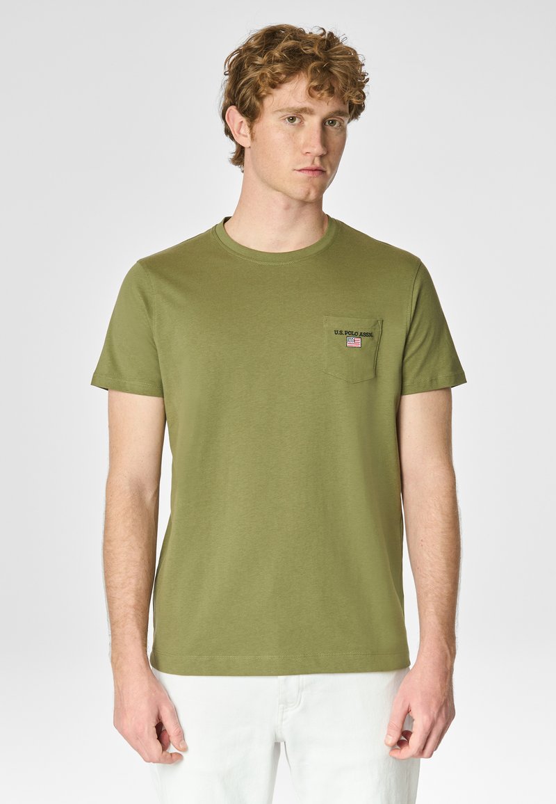T-shirt verde oliva a maniche corte in cotone, con tasca sul petto decorata con un logo e ricamo della bandiera americana. Texture liscia, collo a giro.