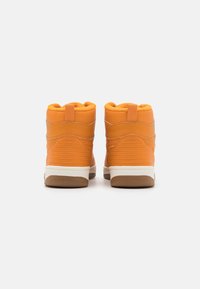 Pomarańczowe sneakersy typu high-top z teksturowanym wykończeniem, wyściełanym kołnierzem i białymi podeszwami. Posiadają wzmocnione szwy i pętlę do zakładania na pięcie.