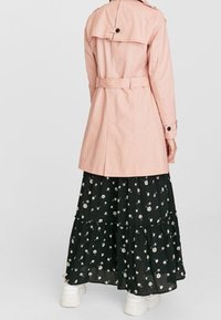 Světle růžový trenčkot s páskem v pase, zadním rozparkem a knoflíkovými detaily, ve spojení s černou květinovou sukní s volány a bílými teniskami.