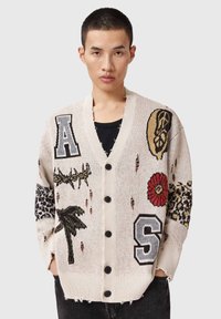Πλεκτή ζακέτα σε κρεμ χρώμα με πολύχρωμα κεντημένα μπαλώματα, περιλαμβάνοντας γράμματα και λουλουδένια σχ έδια. Διαθέτει V-λαιμόκοψη και κλείσιμο με κουμπιά.