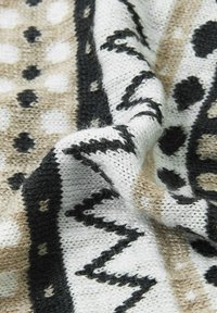 Dzianina z mieszanką białego, czarnego i beżowego, z wzorami kropek, zygzaków i abstrakcyjnych kształtów, ukazująca teksturowane warstwy i fałdy.
